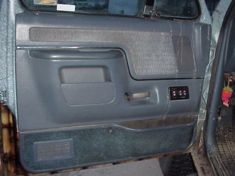 1989 Ford Bronco - Close-up of a gray driver's door panel with a molded map pocket, cloth-textured upper insert, horizontal pull handle and chrome-trimmed int…