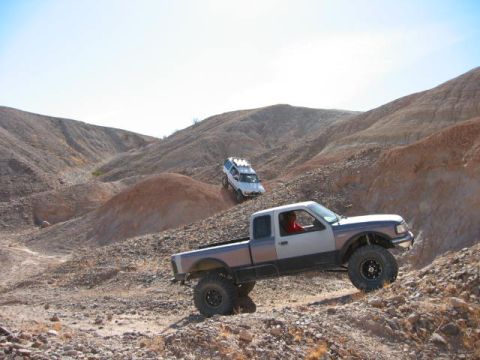 1997 Ford Ranger - A two-tone 1997 Ford Ranger navigates a steep, rocky incline with another off-road vehicle visible in the background.