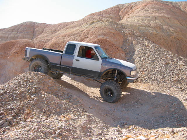 Pickup truck with lifted suspension driving on a dirt hill. Truck has a two-tone paint job