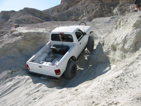 1997 Ford Ranger - A white 1997 Ford Ranger navigates a steep, sandy off-road trail with rocky hills in the background.