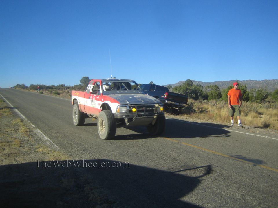 Red, white and blue off-road race truck on rural highway with onlooker