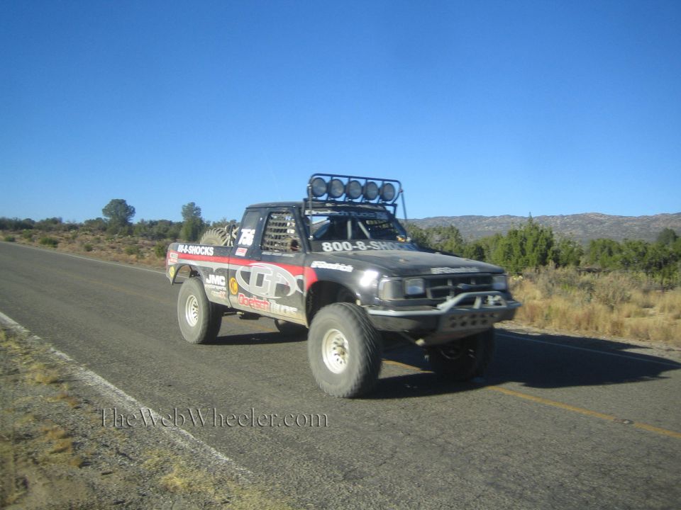 Black off-road race truck with sponsor decals on rural highway