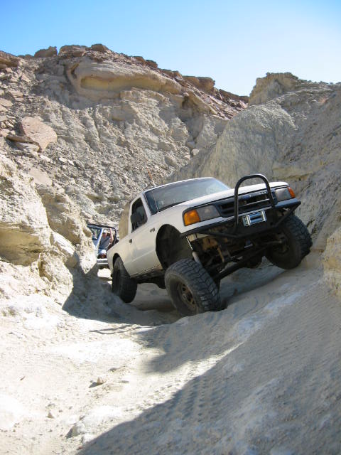 1997 Ford Ranger - Two off-road vehicles navigate a challenging rocky and sandy trail under a clear blue sky.