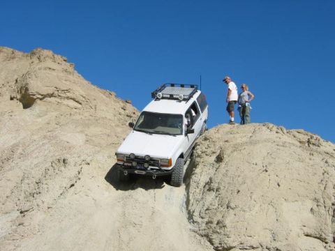 1997 Ford Ranger - A white SUV navigates a challenging off-road terrain under a clear blue sky.