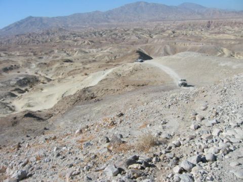 1997 Ford Ranger - Two trucks navigate a dusty road through a barren, mountainous desert landscape under a clear blue sky.