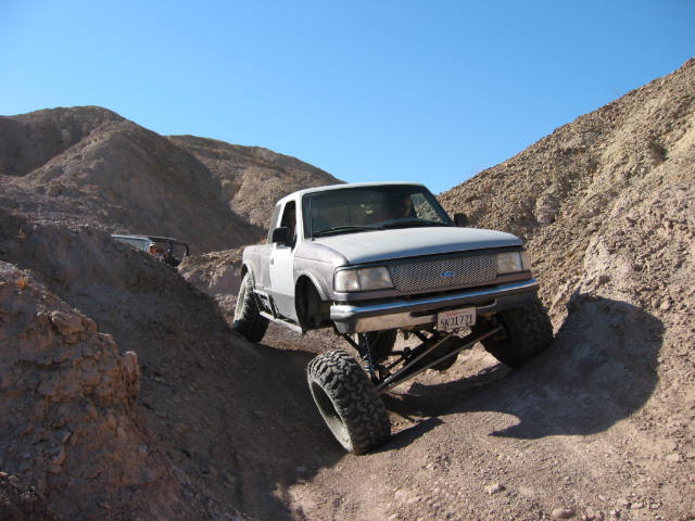 1997 Ford Ranger with lifted suspension and large tires climbing a dirt hill, another vehicle visible behind it
