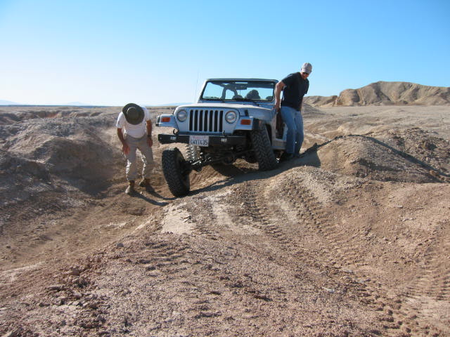 Jeep Wrangler climbing a dirt hill with two people outside
