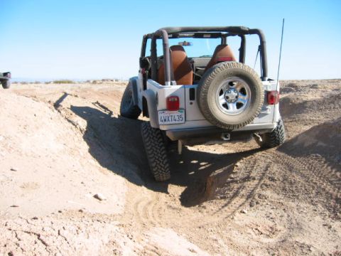 1997 Ford Ranger - A silver Jeep Wrangler navigates a sandy off-road trail under a clear blue sky.