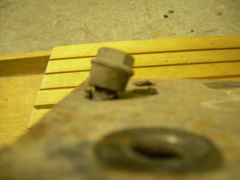 1978 Ford Bronco - Close-up of a rusted metal part with a bolt, likely a motor mount, with wooden planks in the background.