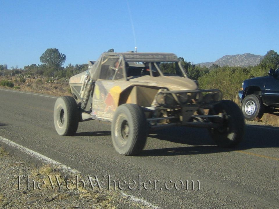 Tan single-seat off-road race buggy driving along a desert highway