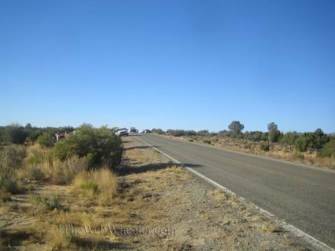 1990 Ford Bronco - two-lane desert highway stretches into the distance under a clear blue sky, with brush along the shoulder and vehicles parked far ahead.