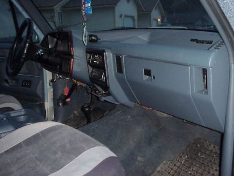 1989 Ford Bronco - Passenger-side view of a gray dashboard with an open glovebox door, center vents and a stereo head unit in the dash stack. The black steeri…
