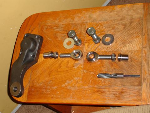 1989 Ford Bronco - Various steering linkage components and a drill bit are laid out on a wooden table.