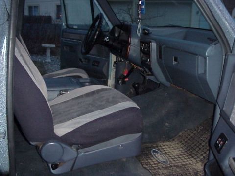 1989 Ford Bronco - Interior shot taken through the open passenger door of a grey 1980s-90s Ford truck cab, showing a two-tone blue and grey cloth split bench…