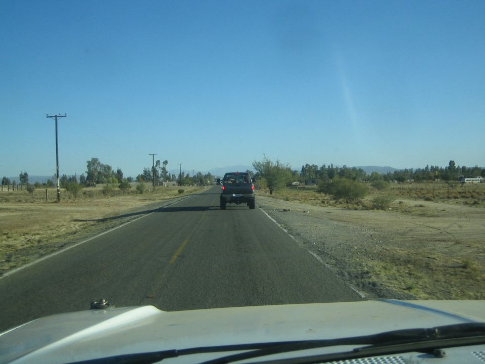 View through a windshield of a dark pickup ahead on a rural paved road