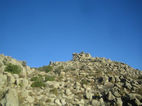1990 Ford Bronco - rocky, boulder-strewn hillside dotted with sparse green shrubs rises against a deep blue cloudless sky.