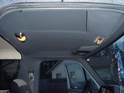 1989 Ford Bronco - Interior view looking up at the gray headliner and dome lights of an SUV with the rear hatch raised, neighborhood visible through the glass.