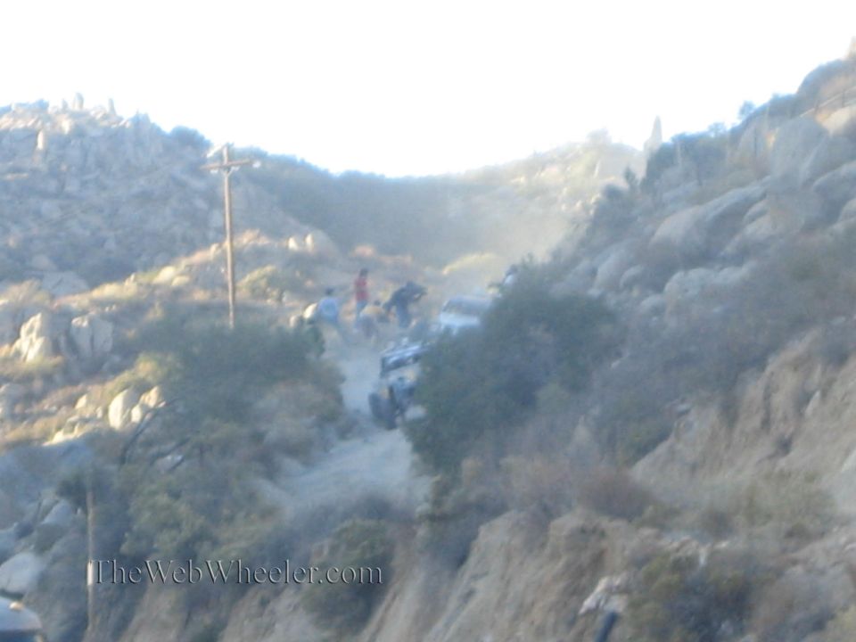 Blurry dusty hillside scene with people and an off-road vehicle on a dirt trail
