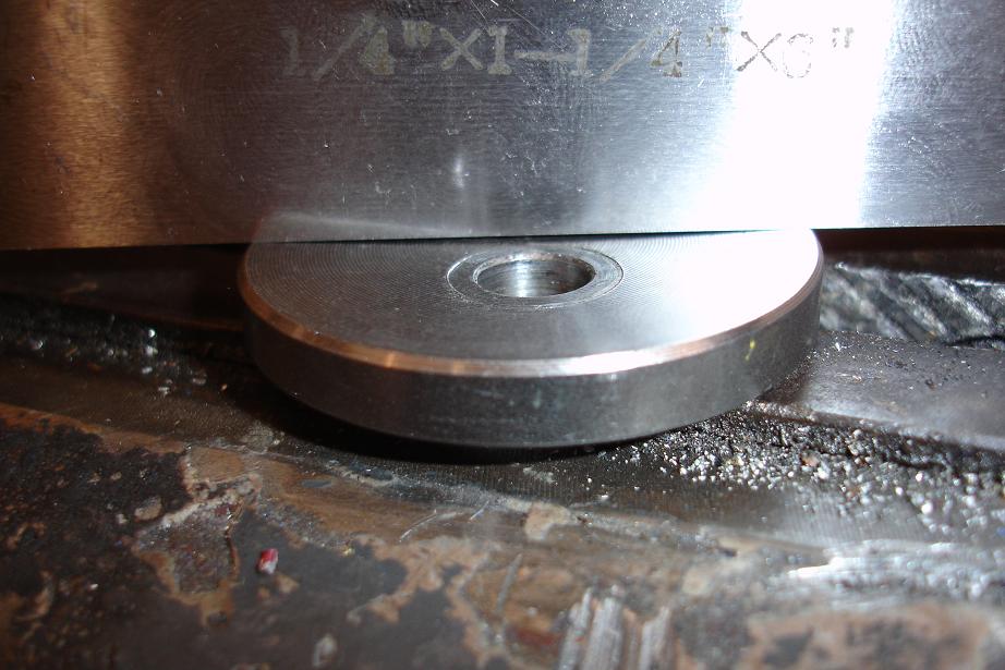 Metal part with engraved text '1/4"X1-1/4"X3"' resting on a rough surface
