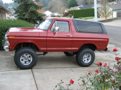 1979 Ford Bronco - This lifted red Ford Bronco, likely a 1978 model, is parked on a paved driveway with a black top.
