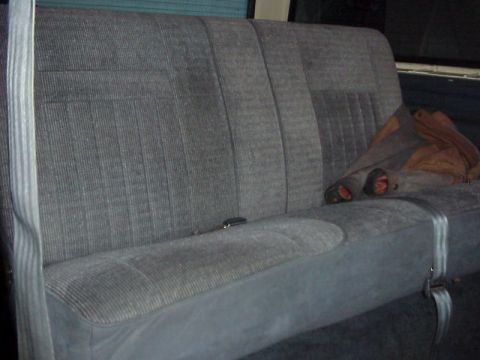 1989 Ford Bronco - Gray cloth rear bench seat inside a Ford truck, photographed from the passenger side with the folding split backrest upright and a seat bel…