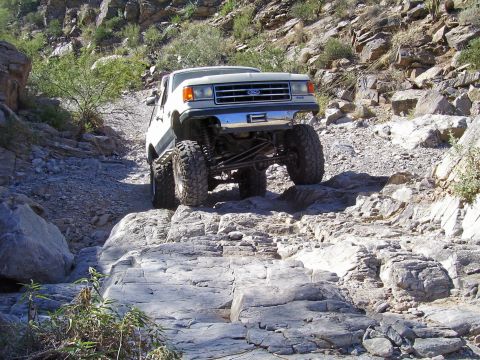 1991 Ford Bronco - A white Ford truck navigates a rocky, off-road trail.