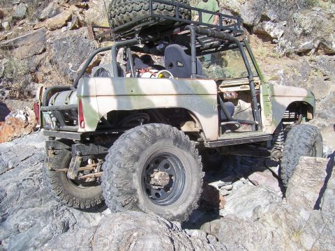 1991 Ford Bronco - This heavily modified SUV, painted in camouflage, navigates a challenging rocky landscape.
