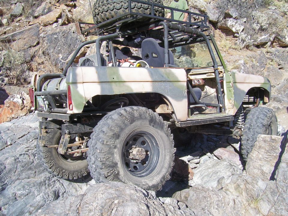 Camouflaged off-road SUV with large tires and roll cage on rocky terrain