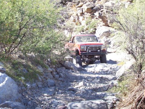 1991 Ford Bronco - Modified red Ford Bronco tackles a challenging rocky path in a desert landscape.