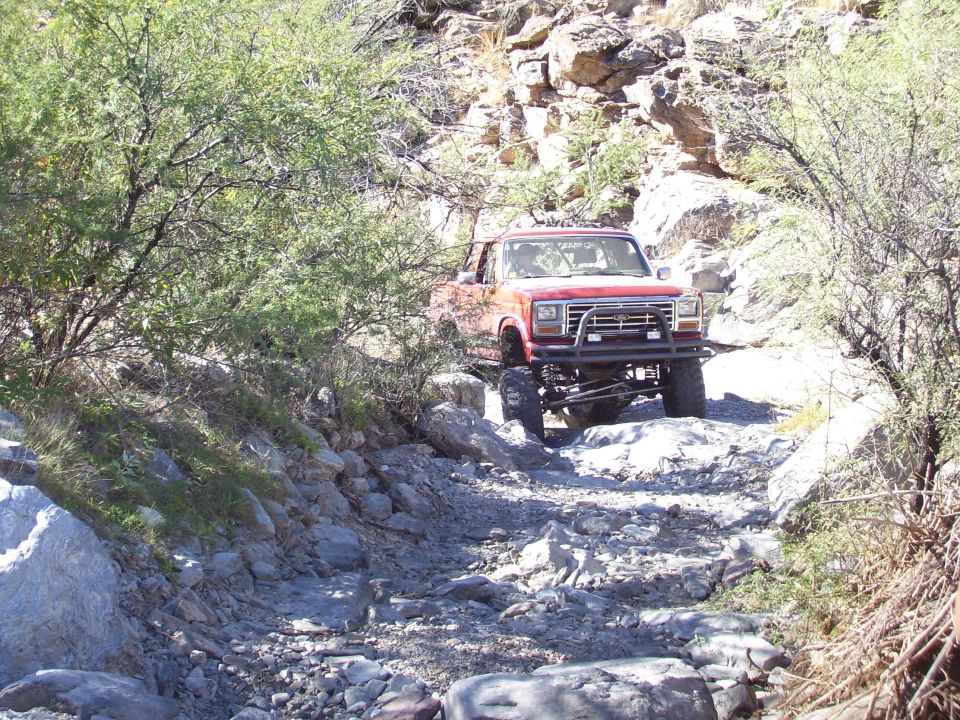 Red Ford Bronco modified for off-roading navigating a rocky trail
