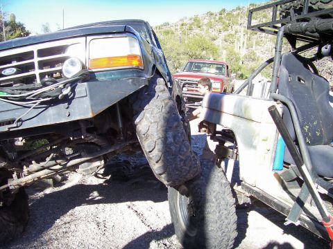 1991 Ford Bronco - Two off-road vehicles are positioned closely together in a desert landscape, with a red pickup truck in the background.