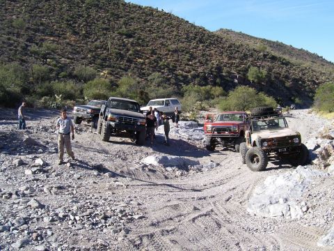 1991 Ford Bronco - Several off-road vehicles are gathered on a rocky terrain under a clear blue sky.
