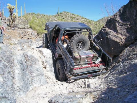 1991 Ford Bronco - This modified SUV is shown navigating a challenging rocky terrain, with its doors open and spare tire mounted at the rear.