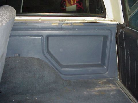 1989 Ford Bronco - Interior view of the rear cargo area passenger-side quarter panel trim, showing a gray molded plastic panel with a recessed storage/access…