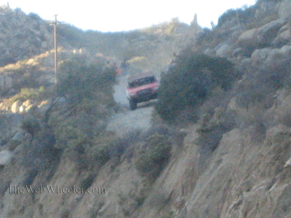 Red off-road race truck climbing a steep dusty hillside trail at dusk
