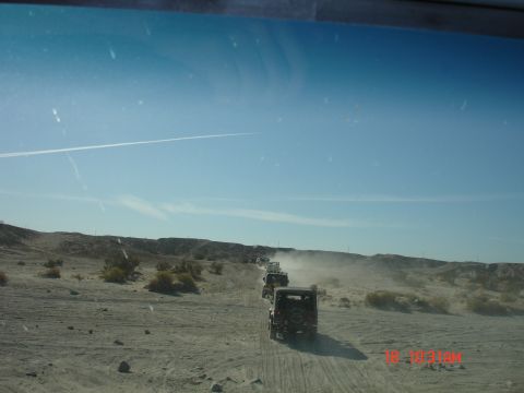 1996 Ford Bronco - A convoy of Jeep Wranglers travels through a dusty desert terrain under a clear blue sky.