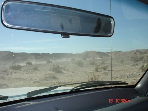 1996 Ford Bronco - Multiple SUVs travel in a dusty convoy across a desert landscape, viewed from inside a vehicle.