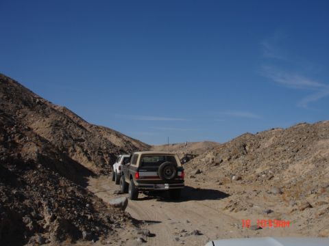 1996 Ford Bronco - Several SUVs, including a 1996 Ford Bronco, travel a dusty path through a rocky desert landscape.