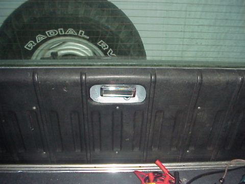 1989 Ford Bronco - Inside of a pickup tailgate with chrome latch handle; a Radial spare tire sits behind the rear window.