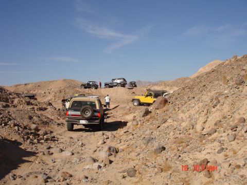 1996 Ford Bronco - A group of SUVs and Jeeps navigate a desert terrain under a clear blue sky.