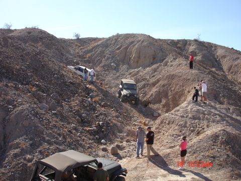 1996 Ford Bronco - Multiple off-road vehicles traverse a challenging, rocky desert landscape under a clear blue sky.
