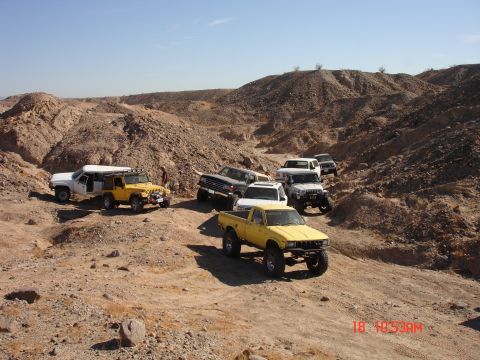 1996 Ford Bronco - Several off-road vehicles navigate a dusty desert terrain under a clear blue sky.