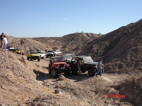 1996 Ford Bronco - A group of off-road vehicles are gathered in a dry, hilly terrain under a clear blue sky.