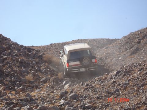 1996 Ford Bronco - A Ford Bronco navigates a steep, rocky incline under a clear blue sky.