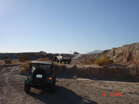 1996 Ford Bronco - Several off-road vehicles traverse a dusty, rocky terrain under a clear blue sky.