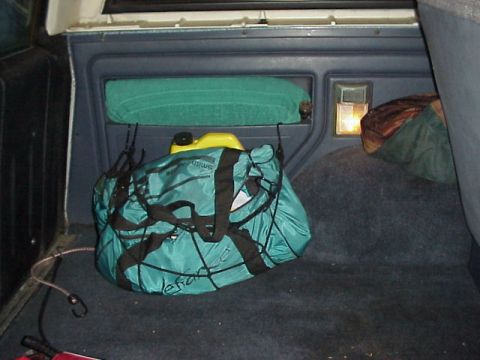 1989 Ford Bronco - Rear cargo area of a full-size SUV shot from the tailgate, showing blue carpeting, a blue plastic quarter trim panel with a storage compart…