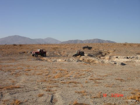 1996 Ford Bronco - Multiple off-road vehicles traverse a desert terrain under a clear blue sky.