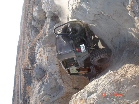 1996 Ford Bronco - A 1996 Ford Bronco is precariously positioned on a steep, rocky incline, with dust rising around it.