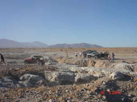 1996 Ford Bronco - Several off-road vehicles are gathered in a rocky desert terrain under a clear blue sky.