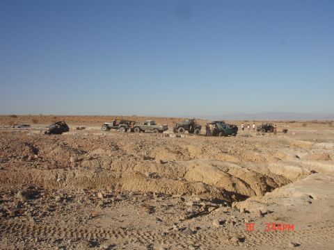 1996 Ford Bronco - A group of off-road vehicles are gathered in a desert area, with a large eroded ditch in the foreground.